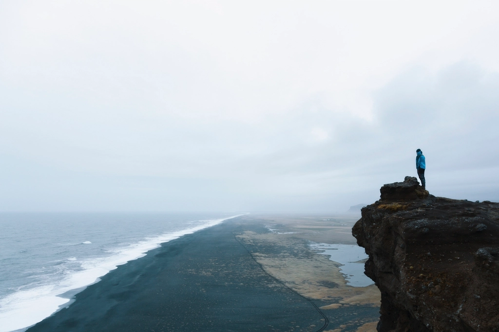 A lone figure on a cliff above an endless coastline