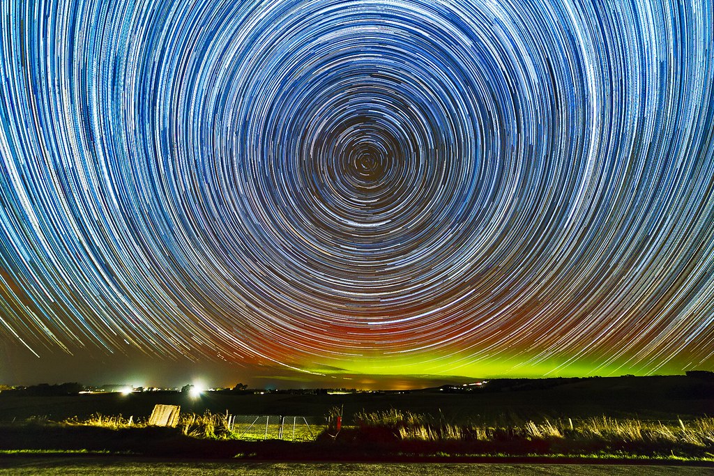 Star trails spinning over an aurora